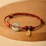Koi fish Hetian jade peace buckle bracelet with red braided cord, cinnabar beads, and engraved gold fortune pendant on wooden surface