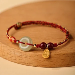 Koi fish Hetian jade peace buckle bracelet with red braided cord, cinnabar beads, and engraved gold fortune pendant on wooden surface