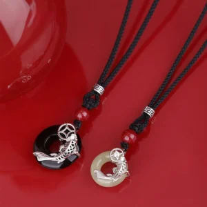 Pair of handcrafted koi fish jade necklaces with black braided cord and silver accents, displayed flat lay on red background