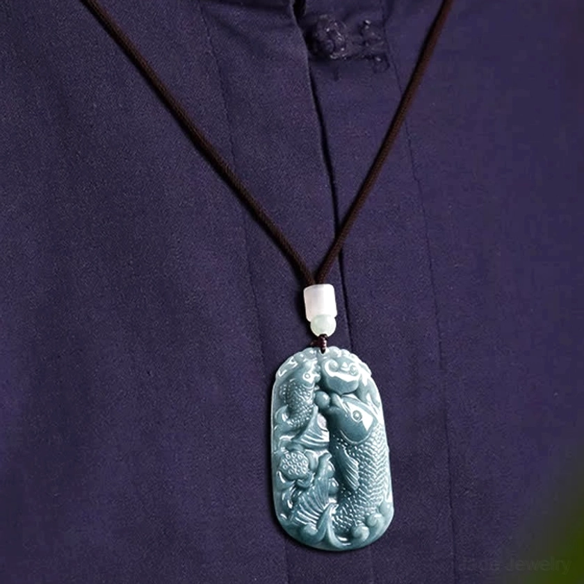 Double koi fish jade pendant necklace worn styling view on dark purple fabric, flat lay showing black beaded cord with white jade bead accent and polished jade pendant