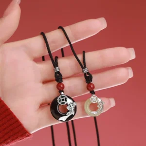Close-up of two koi fish necklaces held in hand, showing silver decorative buckles on braided red cord design
