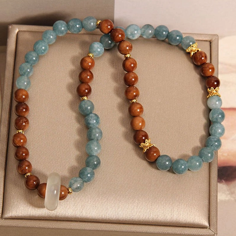 Two separated Kuka Seed Jade bracelets displayed in gift box showing split blue jade strand, brown wooden strand, rectangular white jade pendant, and gold accents