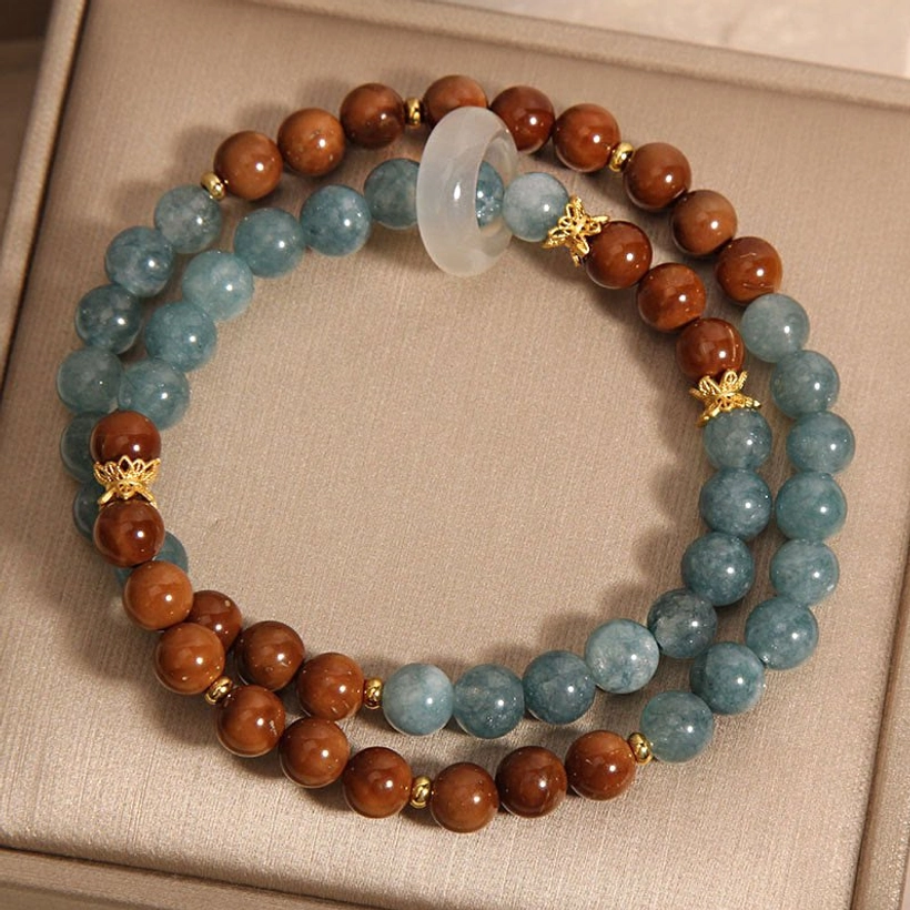 Circular double-layer Kuka Seed Jade wealth bracelet flat lay featuring central white jade donut, gold bead connectors, alternating blue and brown beads in gift box