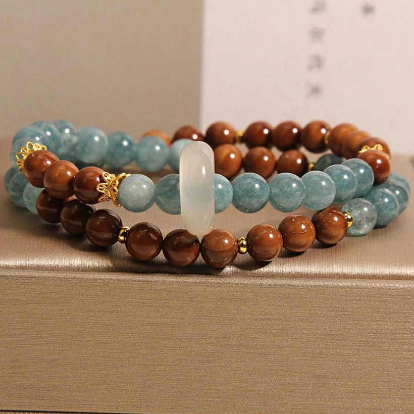 Double-strand Kuka Seed Jade luck bracelet photographed at eye-level showing white jade donut, gold decorative connectors, and mixed blue and brown beads