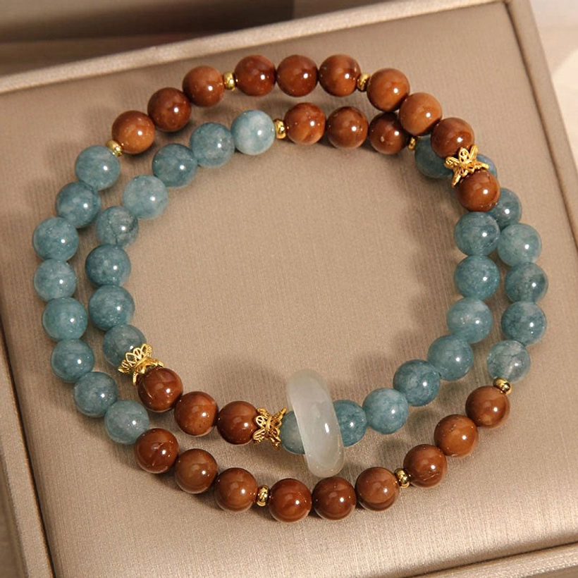 Single Kuka Seed Jade mixed bead bracelet flat lay in gift box showing central white jade pendant, gold bead spacers, alternating blue and brown beads