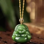 Laughing Buddha cyan jade pendant necklace with 925 silver and 18K gold clasp displayed on wooden surface with natural green foliage background