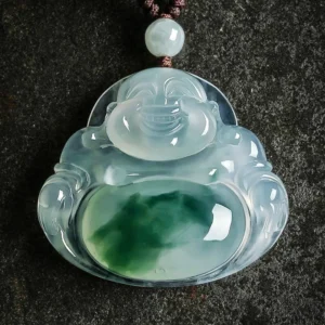 Laughing Buddha Maitreya cyan jade pendant necklace in flat lay composition with braided cotton cord and jade bead accent on dark textured stone surface, showing translucent ice blue jade with green belly patch