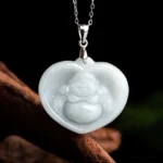 Heart-shaped laughing Buddha white jade pendant necklace with titanium steel chain, front flat view on dark wooden backdrop