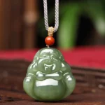 Laughing Buddha Hetian jade pendant necklace frontal view with grey rope and red agate bead on wooden surface with red mat