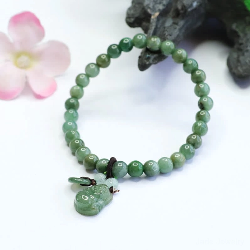 Natural cyan jade beaded bracelet with Laughing Buddha charm and dark knot fastener on decorative rock background