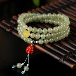Laughing Buddha jade prosperity bracelet multi-loop design with light green jade beads, amber spacer bead, red Buddha pendant, and turquoise tassel on dark bamboo tray