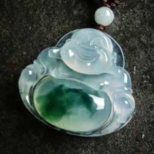 Close-up hand-carved detail of Laughing Buddha jade pendant displaying intricate smiling Maitreya face, polished translucent cyan jade stone, and natural green jade inclusions throughout