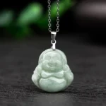 Laughing Buddha jade pendant necklace front view with light green natural jade Maitreya Buddha carving and silver titanium steel curb chain on dark wood background