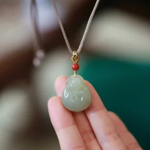 Laughing Buddha Hetian jade pendant held in palm, showing carved details with red bead and gold-toned connector