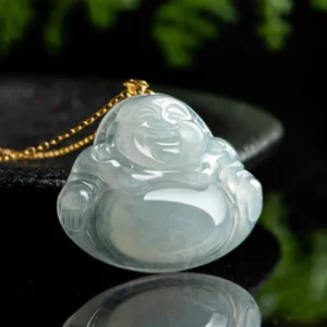 Laughing Buddha jade pendant necklace side angle view with gold chain against dark tableware and green foliage background, highlighting the carved Buddha's profile