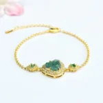Laughing Buddha green jade bracelet with zircon accents on pink floral background, top-down flat lay view