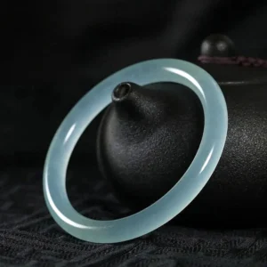Light blue jade bangle bracelet displayed with traditional teapot, showing polished smooth surface and translucent stone quality