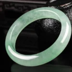 Light green jade bangle bracelet with natural veining, polished finish, three-quarter view showing elegant round design