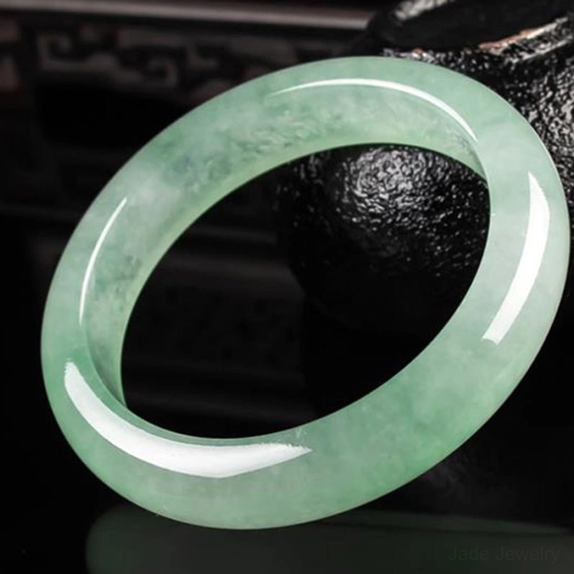 Light green jade bangle bracelet with natural veining, polished finish, three-quarter view showing elegant round design