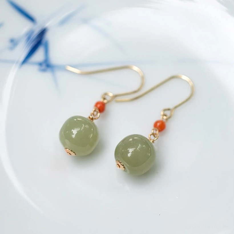 Paired hetian jade drop dangle earrings in light green with red agate beads arranged on blue and white porcelain plate
