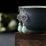 Magnolia jade drop earrings side view with pale green teardrop stones and antique silver flower charms displayed on dark ceramic