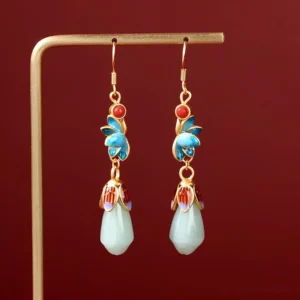 Magnolia jade drop dangle earrings with blue enamel flowers, gold ear hooks, and light green jade buds displayed on metal rack