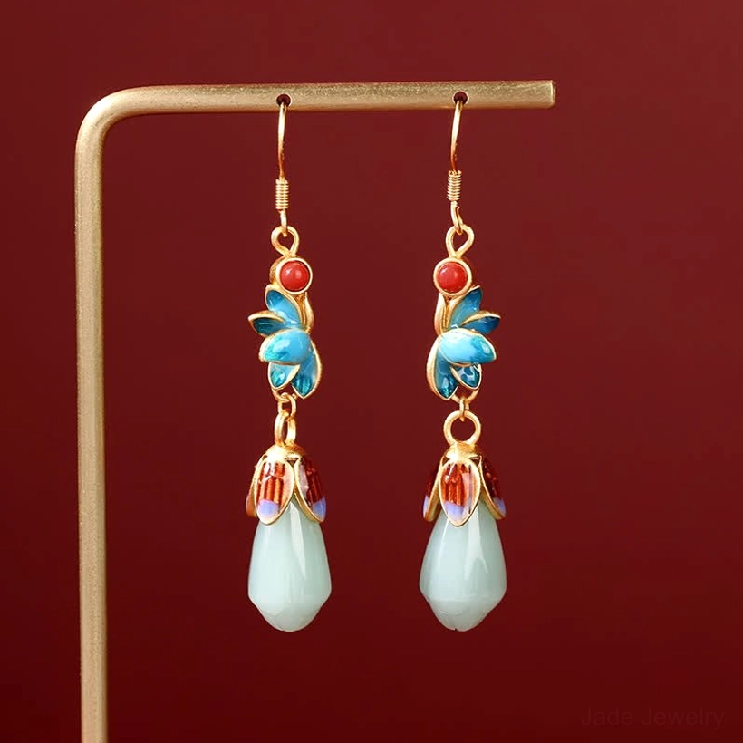 Magnolia jade drop dangle earrings with blue enamel flowers, gold ear hooks, and light green jade buds displayed on metal rack