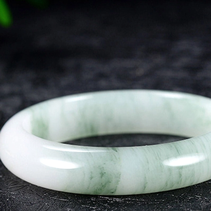 Green-white marbled jade bangle bracelet in three-quarter side view showcasing natural stone grain and lustrous finish