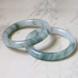 Pair of matching natural jade bangles with dark green flower patterns displayed on light table surface, flat lay top view showing polished finish