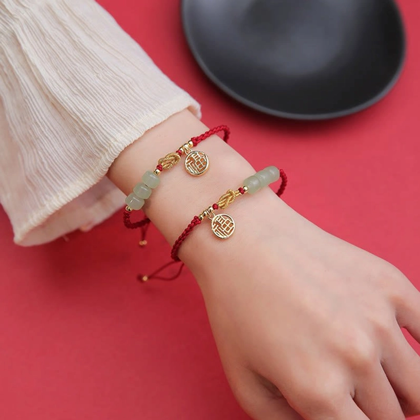 Two matching handcrafted jade Fu bracelets worn on dual wrists with white long sleeve shirt - paired styling on red background