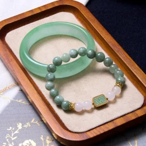 Mint green jade bangle with white agate and jade beaded bracelet bundle displayed on wooden tray with fabric mat