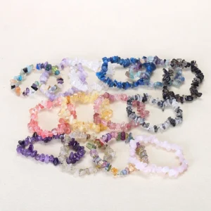 Assorted irregular chip stone healing bracelets flat lay on beige background, various natural crystal color options