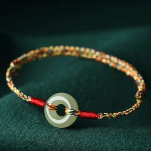 Multicolor woven jade peace buckle bracelet with vibrant rope detail on dark green fabric, overhead close-up view