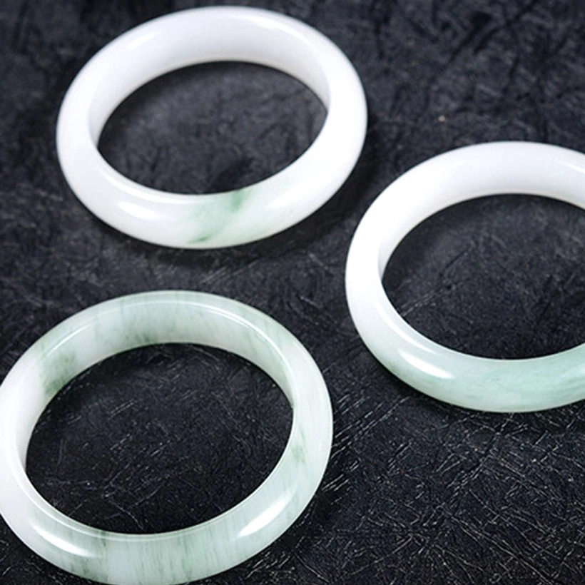 Multiple jade bangles flat overhead arrangement showing variety of natural colors including green-veined and white options