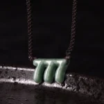 Green jade 777 angel number pendant necklace close-up top view showing carved triple seven charm with dark brown hand-braided adjustable cord