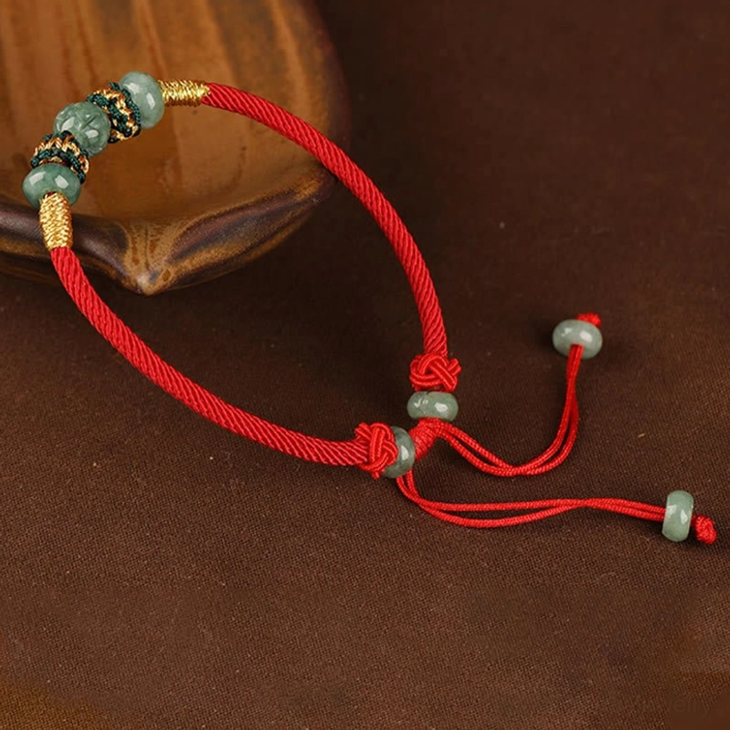 Natural green jade beads on red prosperity bracelet showcasing color variation and authentic stone texture