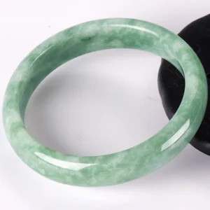Overhead flat lay of natural jade bangle bracelet with light green marbled pattern and polished smooth finish on white background, clearly showing inner diameter and jade quality