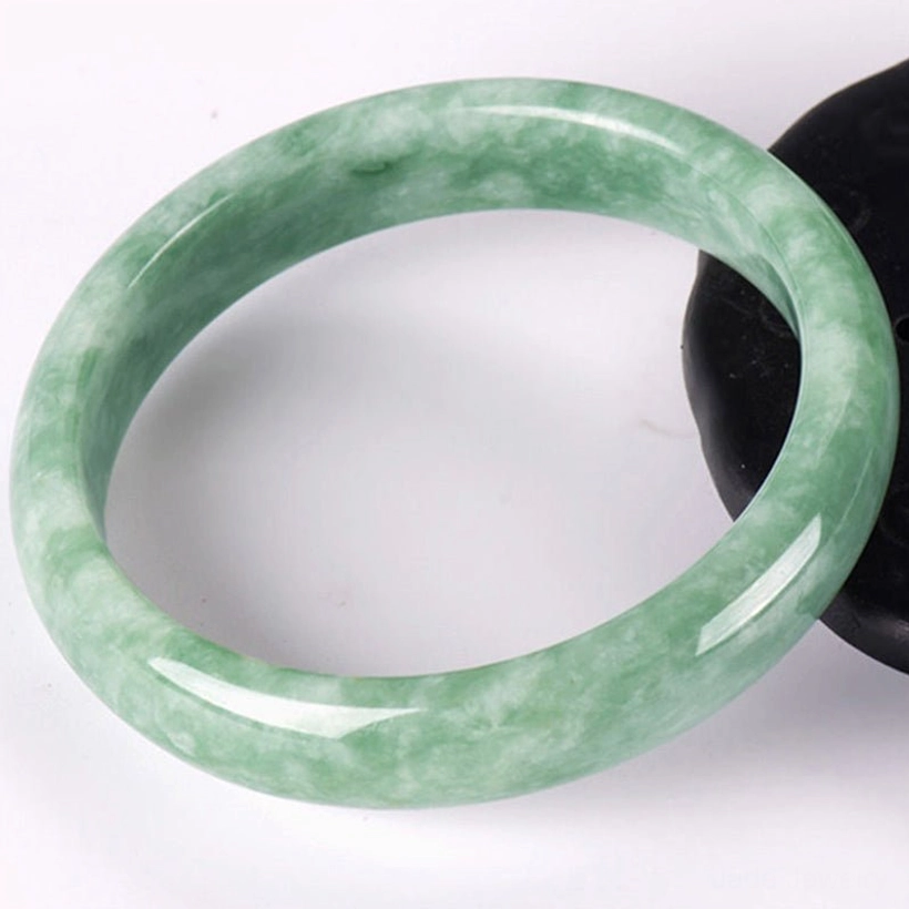 Overhead flat lay of natural jade bangle bracelet with light green marbled pattern and polished smooth finish on white background, clearly showing inner diameter and jade quality