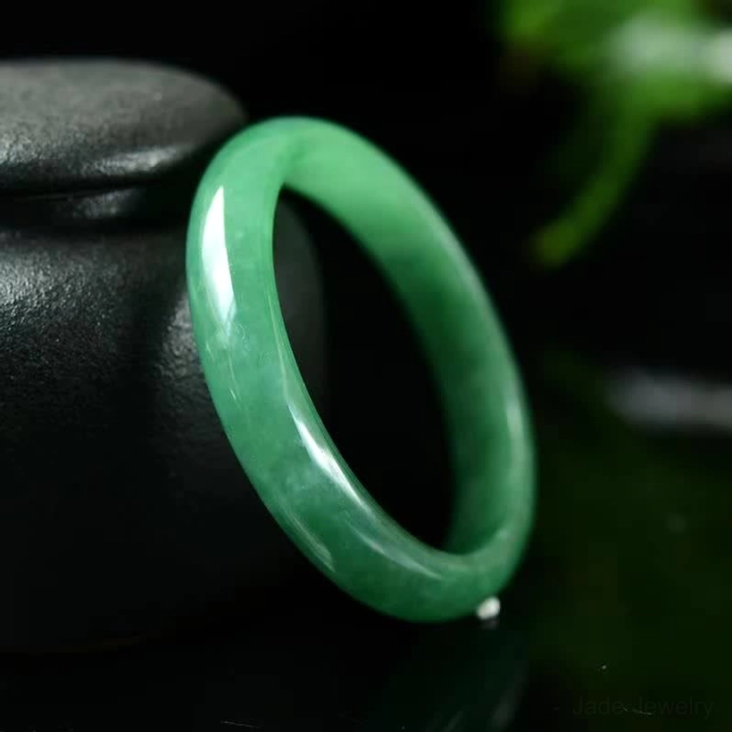 Natural green jade bangle bracelet with smooth polished finish, side oblique view showcasing deep emerald color and lustrous surface quality
