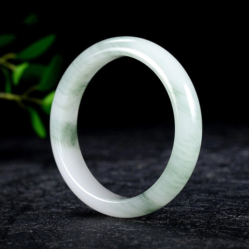Natural jade bangle bracelet three-quarter view showing polished green and white marbled pattern on dark stone background