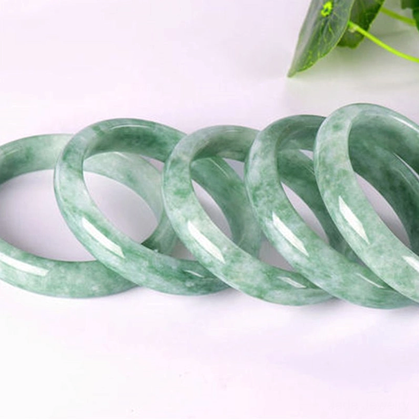 Multiple natural jade bangles set displaying uniform light green mottled jade finish on light pink background with green leaf decoration, showing size and style consistency