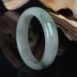 Natural jade bangle bracelet with light green base and dark green veining, polished finish side profile view