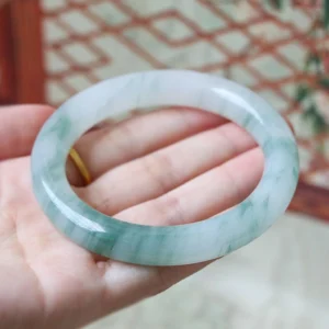 Natural jade bangle bracelet with dark green veining held in palm, close-up view showing smooth polished surface and authentic pale jade base