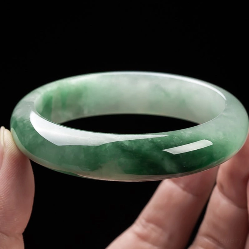 Close-up of natural jade bangle held by fingertips displaying light green base with dark green natural streaks