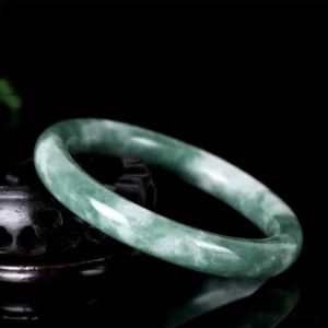 Authentic jade bangle bracelet three-quarter side view on dark wooden holder, showcasing polished green-white texture