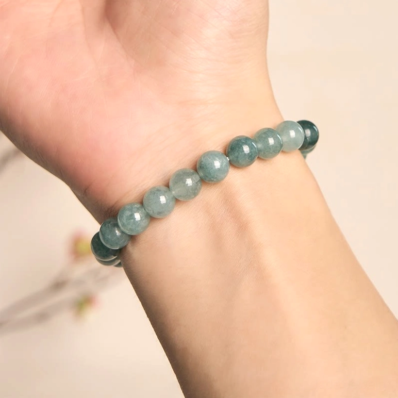 Dark teal jade beaded bracelet worn on left wrist in indoor lifestyle setting, handmade natural stone bracelet without charm