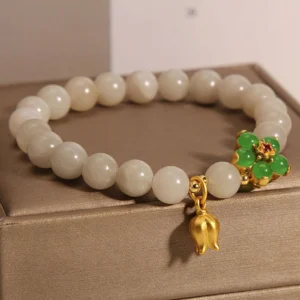 Handmade jade beaded lucky bracelet side view displaying smooth off-white beads with green floral ornament and gold lily charm on jewelry tray