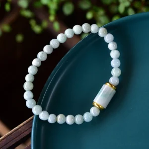 Handcrafted jade bracelet side angle view displaying matte light green beads and gold-trimmed central tube bead against wooden backdrop