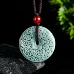 Natural green jade carved peace buckle pendant necklace with intricate floral scroll patterns displayed on dark stone with green foliage