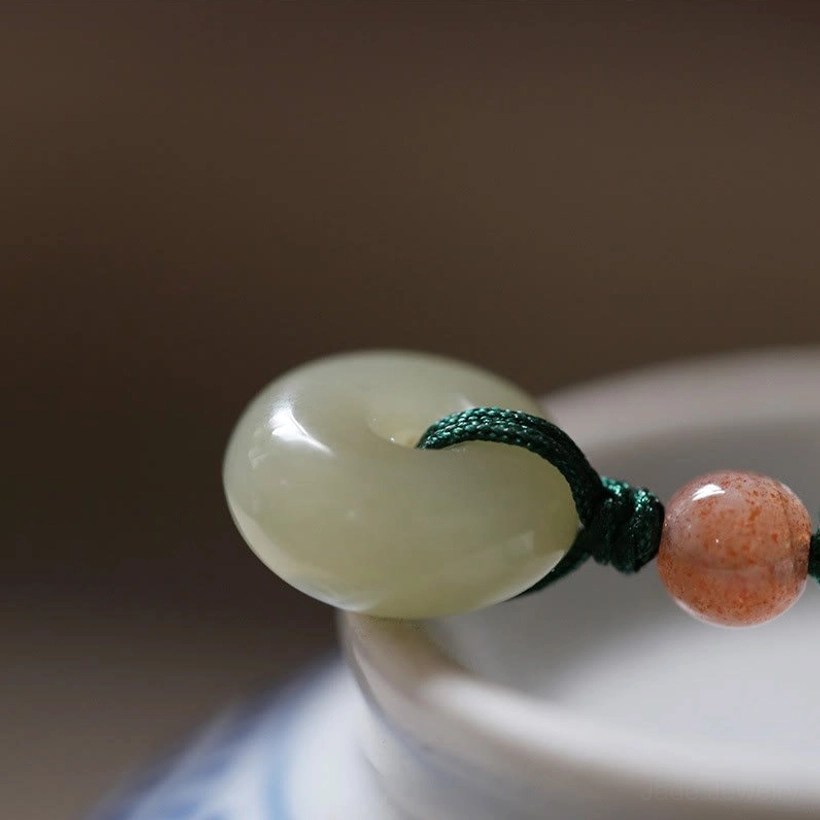 Single carved jade peace buckle pendant with pink accent bead on porcelain display, side view